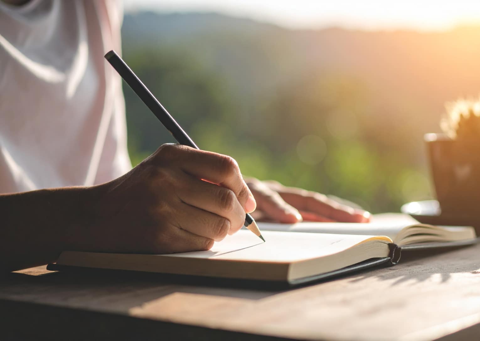 Une main qui écrit dans un carnet, en pleine nature au soleil couchant